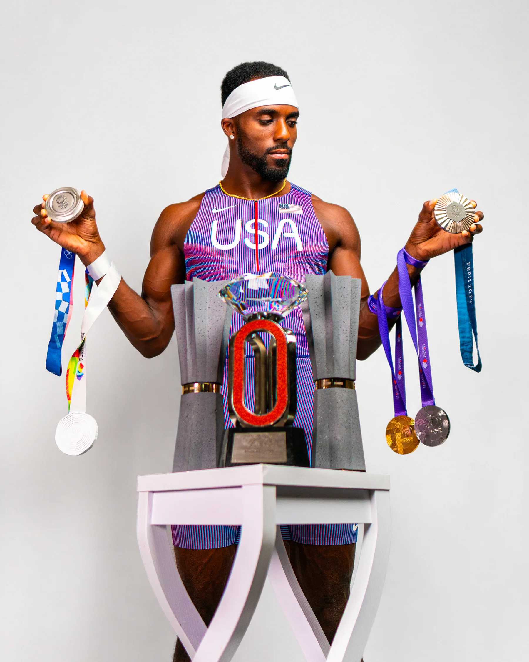 Kenny Bednarek holding his medals behind his championship trophies